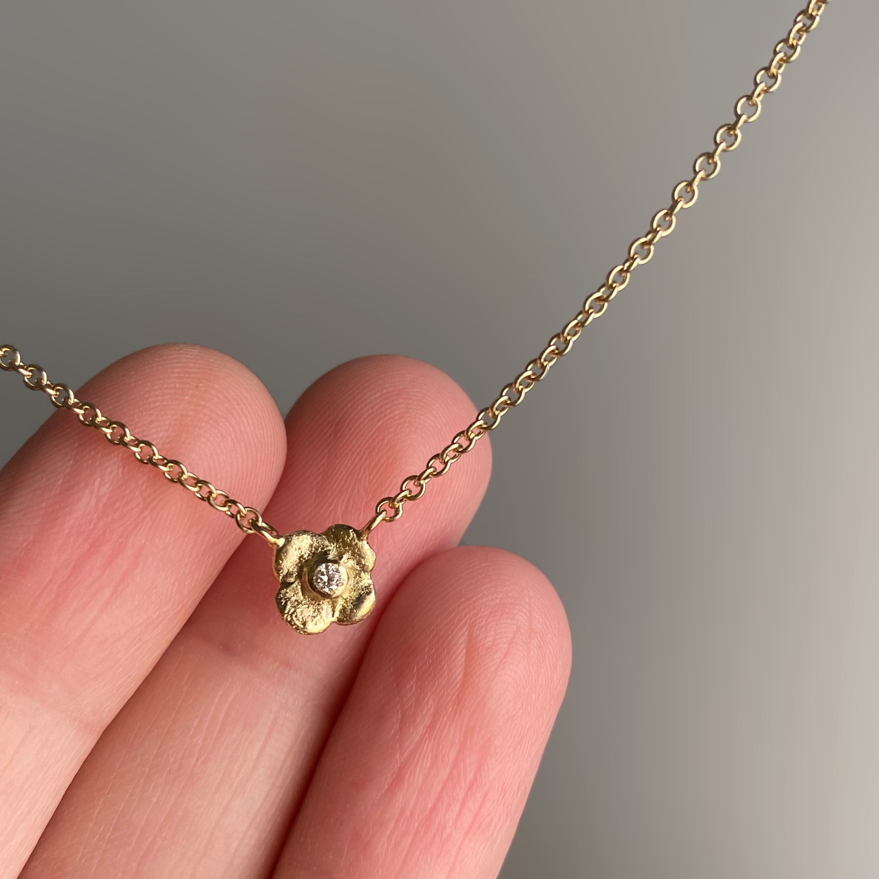 three fingers holding a 14 karat gold flower necklace with a diamond in the middle