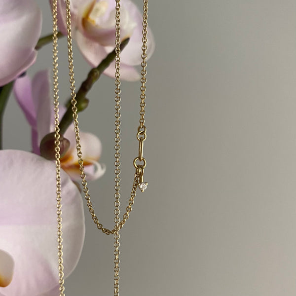 a gold chain with handmade links and a round diamond, orchids in the background