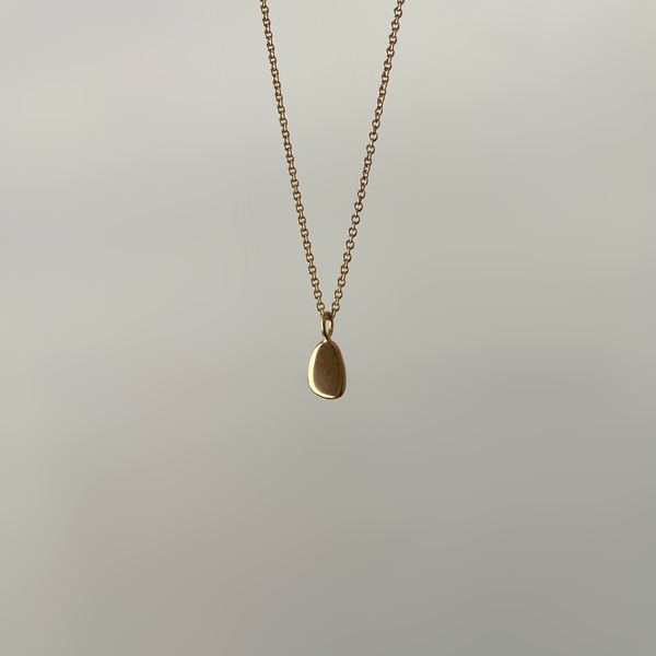 an amorphous 14 karat gold pendant, hung on a gold chain, on white background