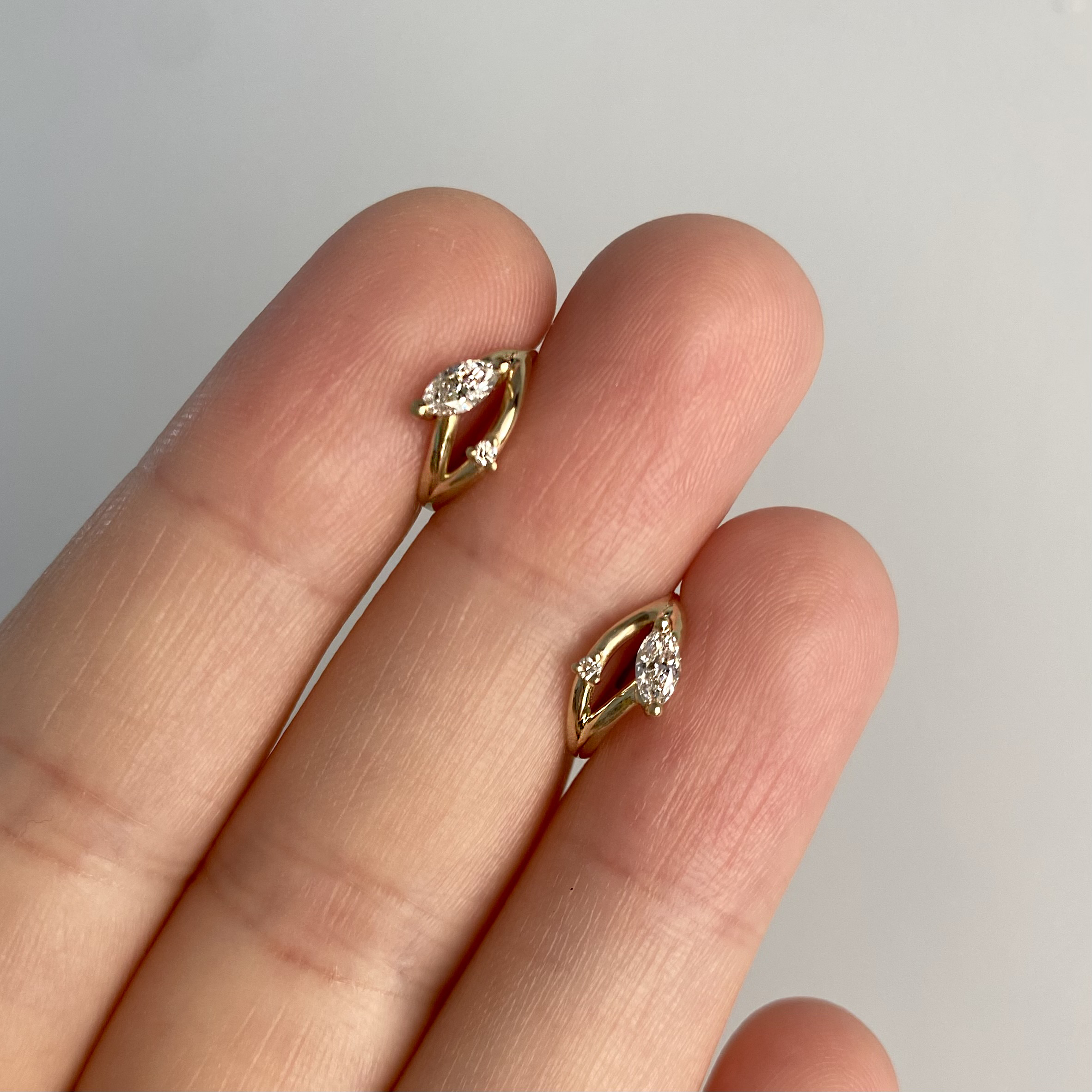 a close-up of a hand holding two 14 karat gold hoop earrings set with diamonds