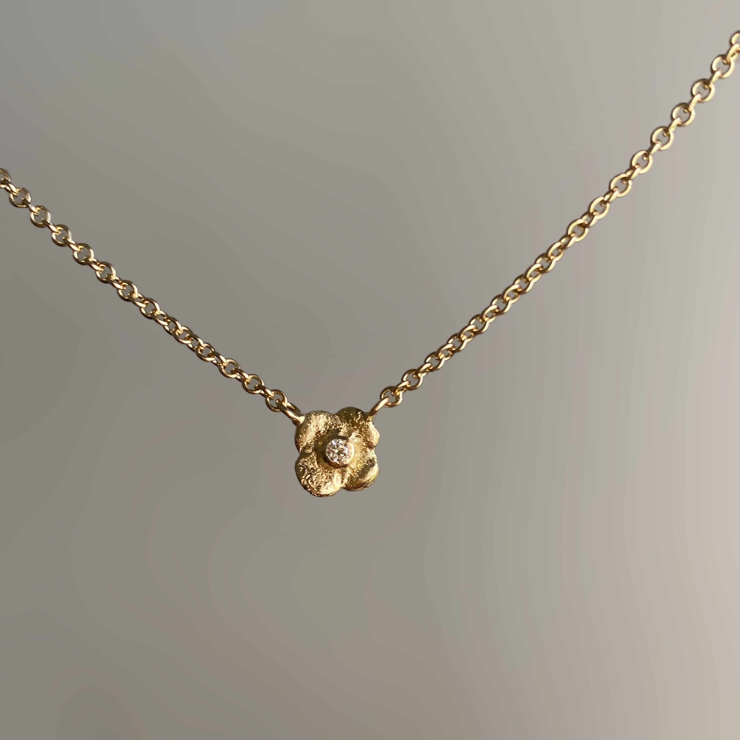 a gold flower pendant set with a round diamond in the middle, hung on a gold chain. white background