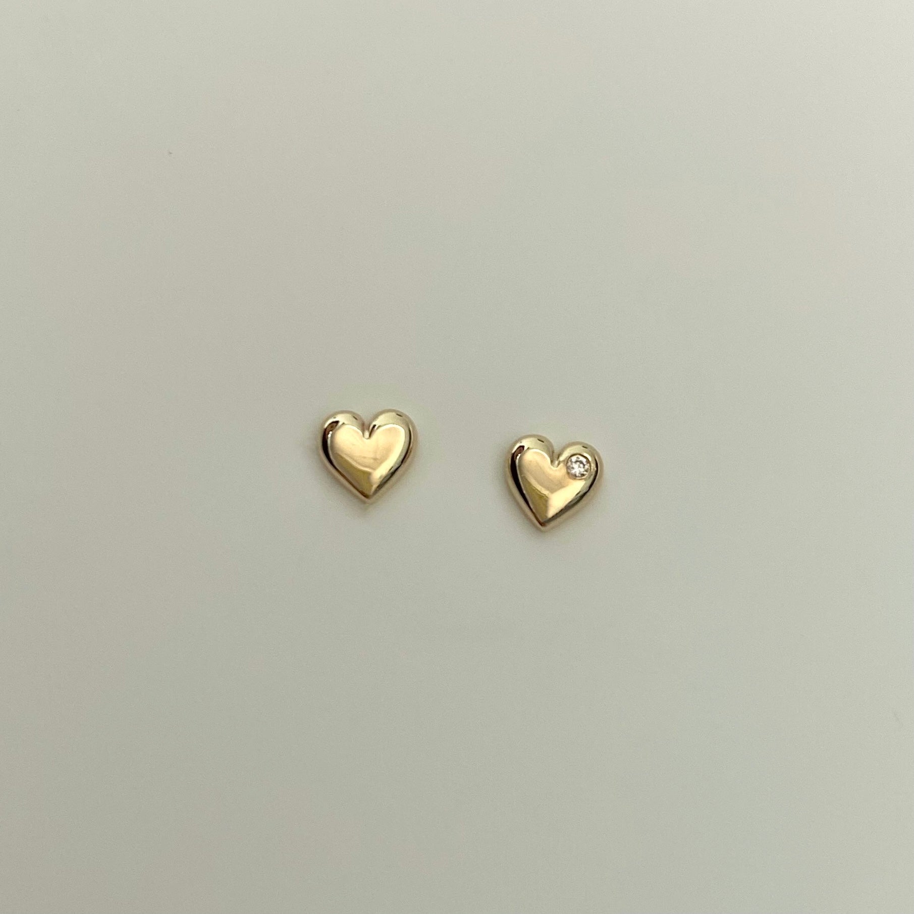 two 14 karat gold heart studs, one is set with a small diamond