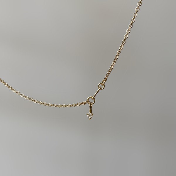 a 14 karat gold necklace with a round white diamond on white background
