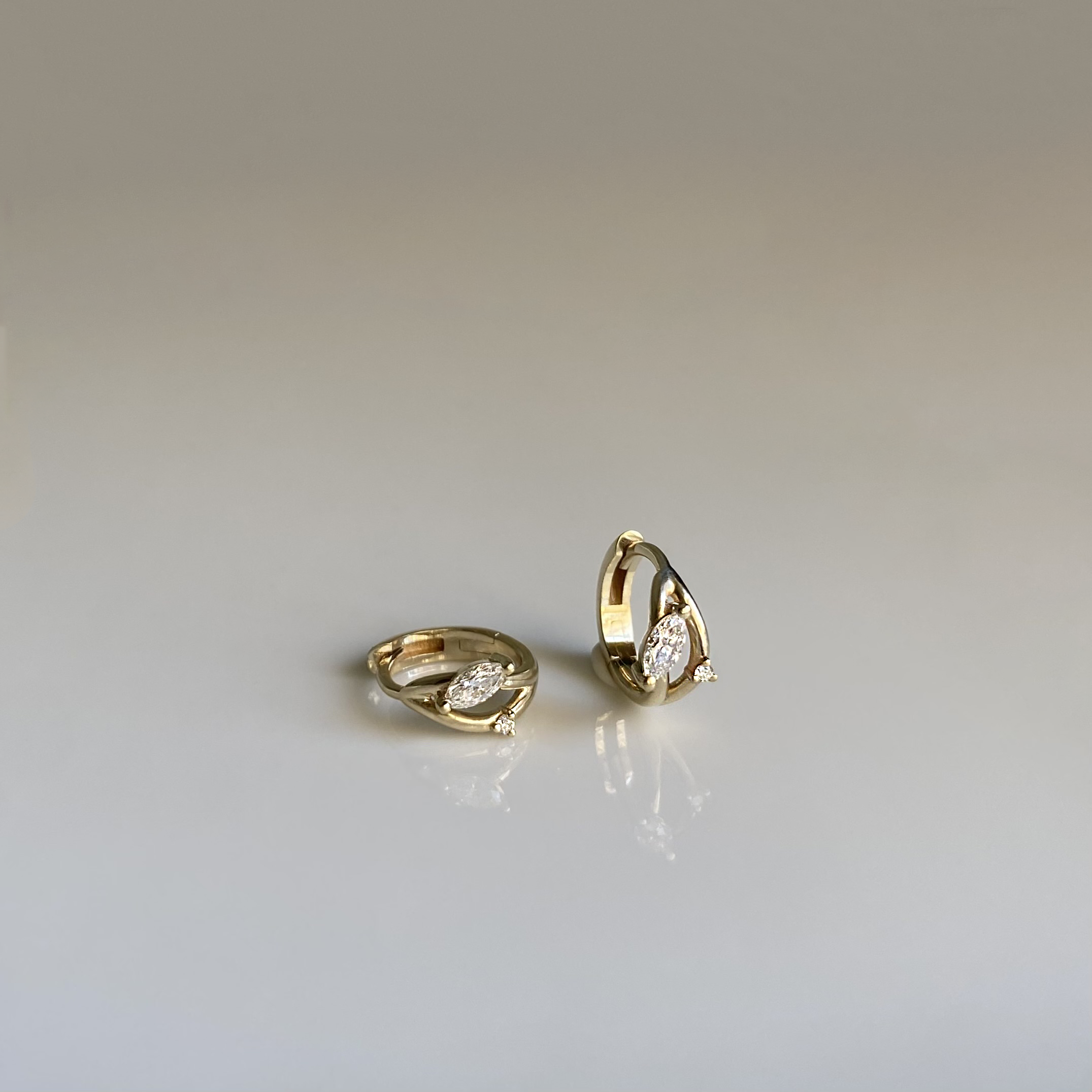 two gold hoop earrings with marquise and round shaped diamonds on white background