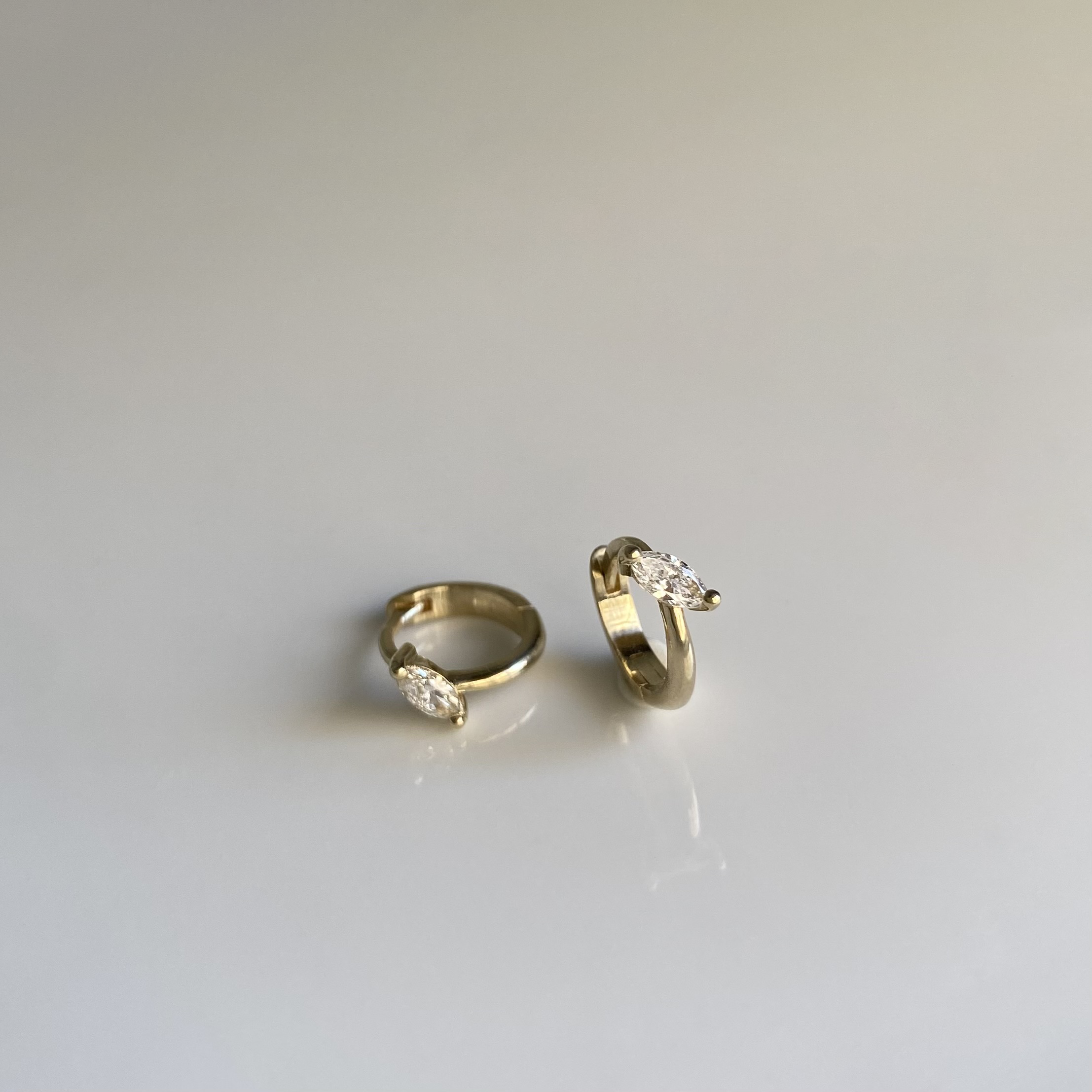 two small huggie earrings with a marquise diamond set in each of them, on a white background