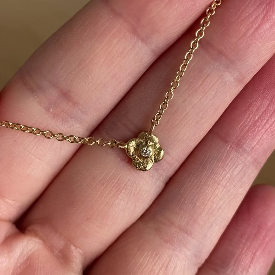 a close-up of a hand holding a 14 karat gold necklace with a four-leaf flower pendant, set with a round diamond