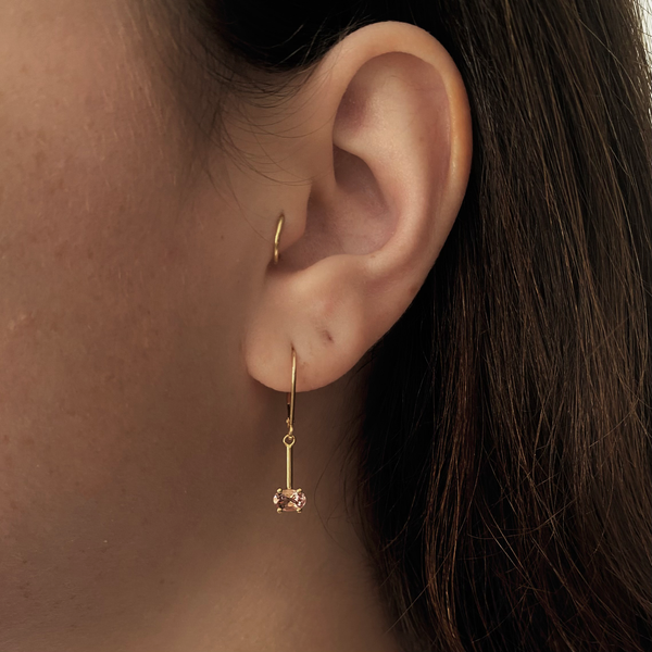 a woman wearing a yellow gold earring with a pink morganite gemstone