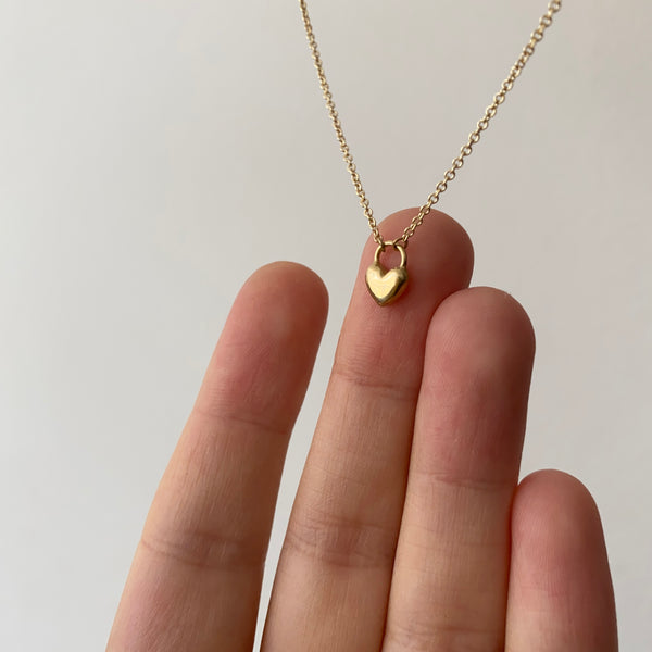 a hand holding a dainty gold necklace with a heart pendant