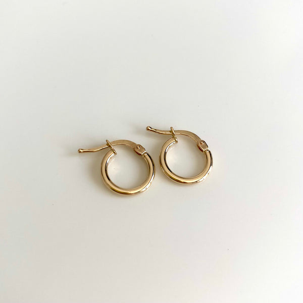 two dainty 14 karat gold hoop earrings on a white background