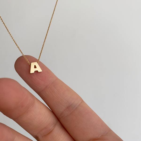 a hand holding a 14 karat gold letter "A" pendant on a white background