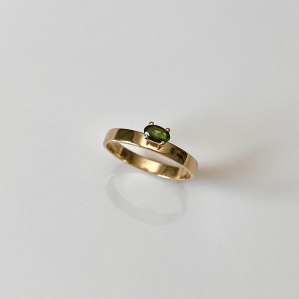 a dainty gold band with a green tourmaline gemstone on white background